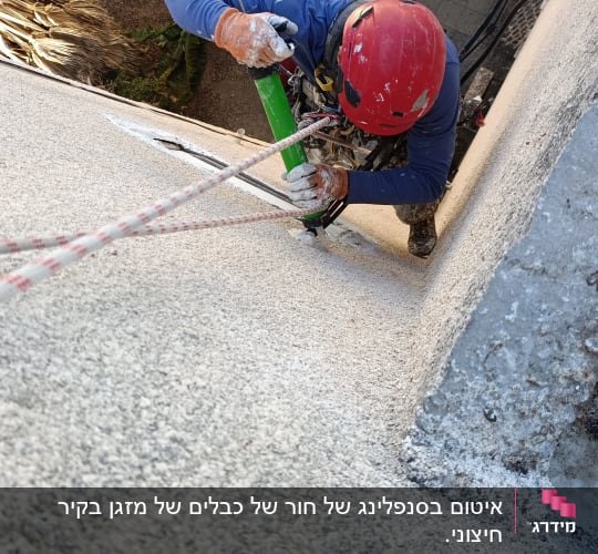 עובד בגובה עם קסדה אדומה מבצע עבודת תחזוקה על קיר חיצוני